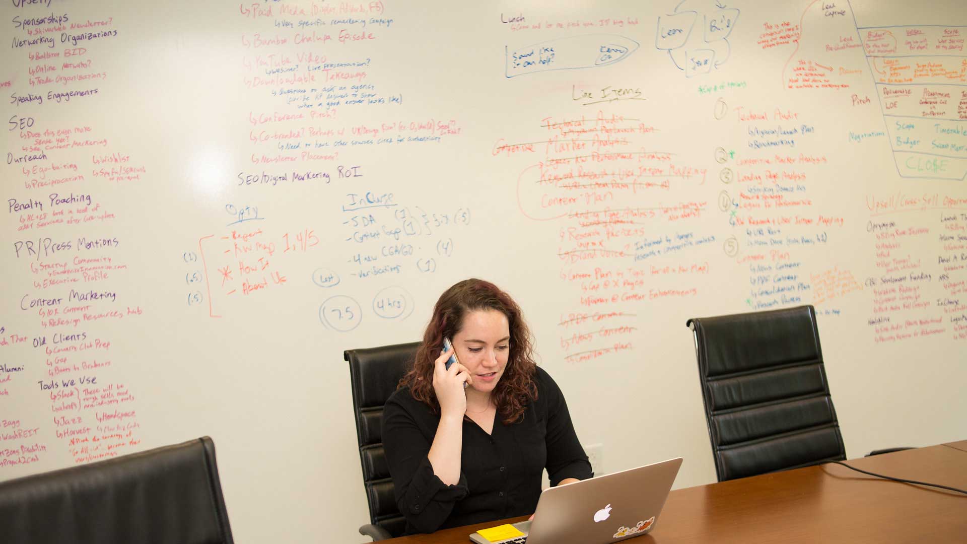 white woman talking on phone with white board in background 