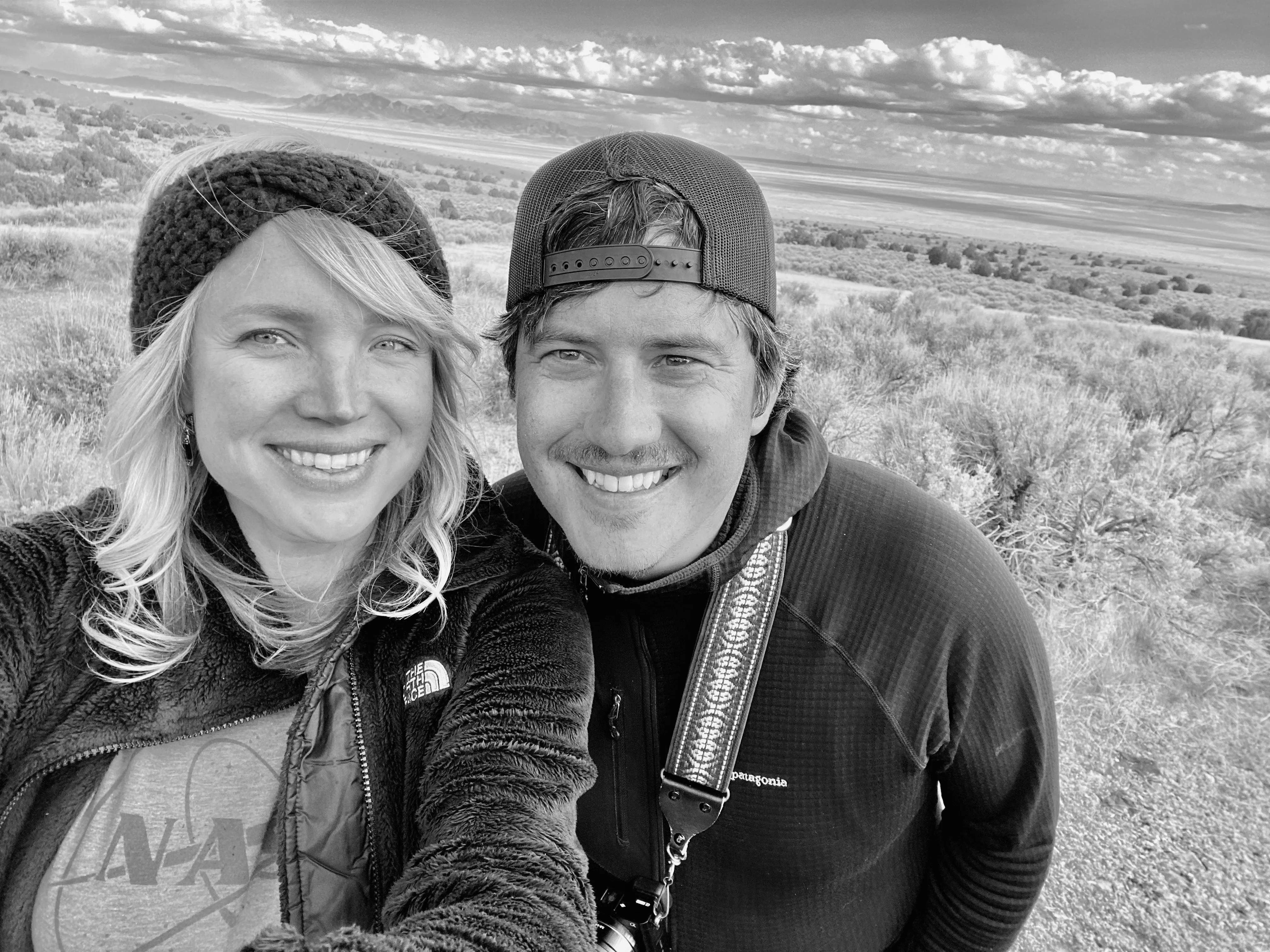 Black and white selfie of Geoff and Whitney smiling outdoors in a mountain sagebrush landscape